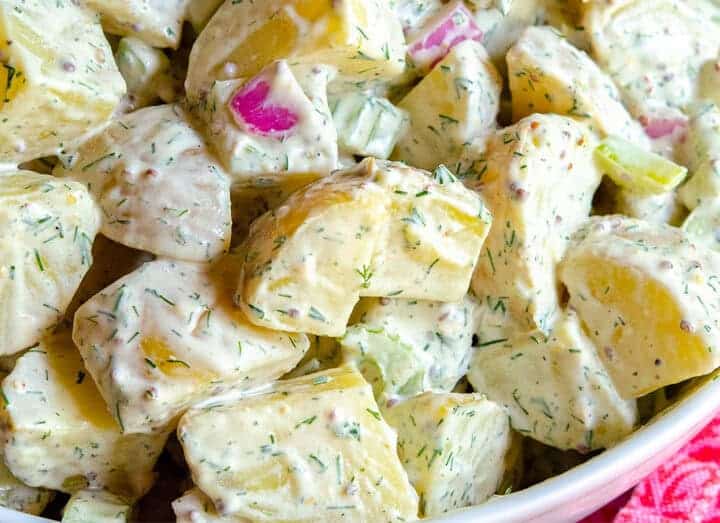 A close-up of a bowl of creamy potato salad with chopped potatoes, celery, red onion, and fresh herbs-an ideal side when wondering what to serve with chicken drumsticks.