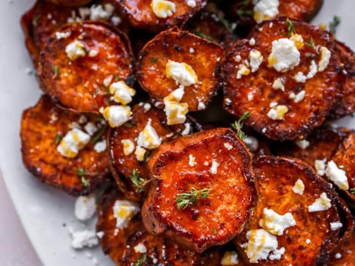 A plate of roasted sweet potato rounds topped with crumbled feta cheese and fresh herbs-an irresistible side dish for what to serve with chicken drumsticks.