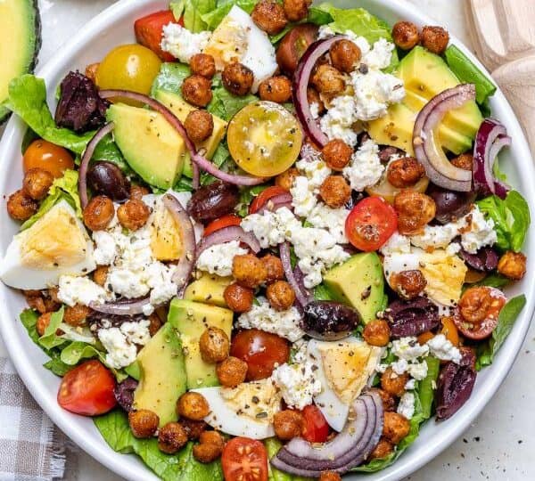A salad with lettuce, cherry tomatoes, avocado, red onion, hard-boiled eggs, chickpeas, feta cheese, and olives in a white bowl-perfect if you're wondering what to serve with chicken drumsticks.