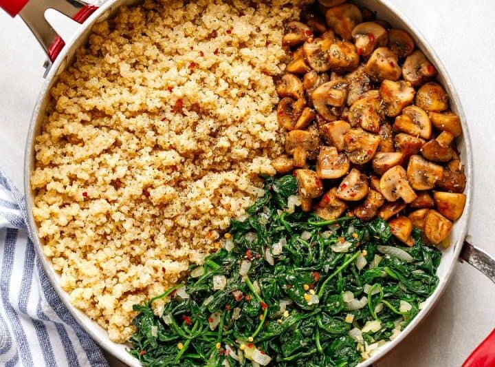 A skillet containing cooked quinoa, sautéed mushrooms, and wilted spinach with onions-each arranged in separate sections-makes a wholesome side if you're wondering what to serve with chicken drumsticks.
