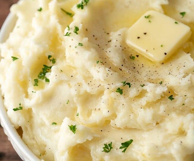 A bowl of mashed potatoes topped with a pat of butter, chopped parsley, and a sprinkle of black pepper-perfect for what to serve with chicken drumsticks.