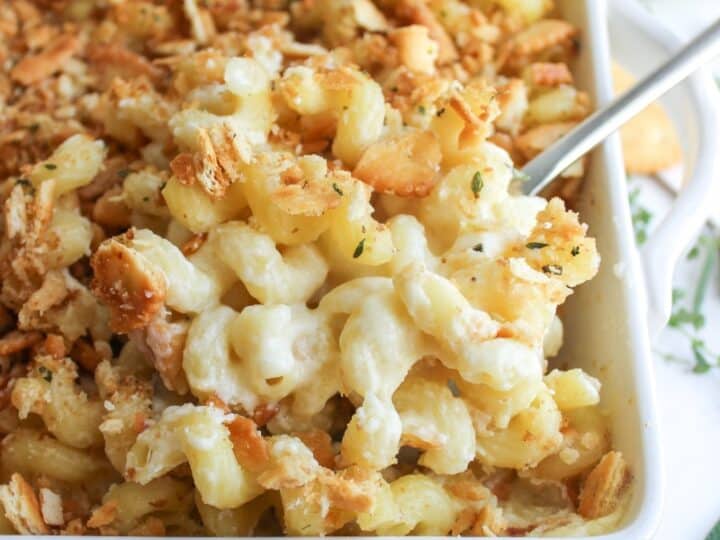 Baked macaroni and cheese in a white dish, topped with golden breadcrumbs, with a serving spoon scooping out a portion-an ideal comfort side when deciding what to serve with chicken drumsticks.