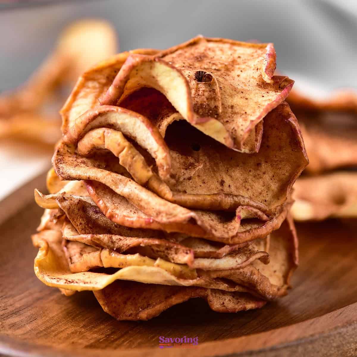 Close-up of a stack of air fried apple chips on a wooden surface. The apple slices are seasoned with cinnamon and have a crispy texture.