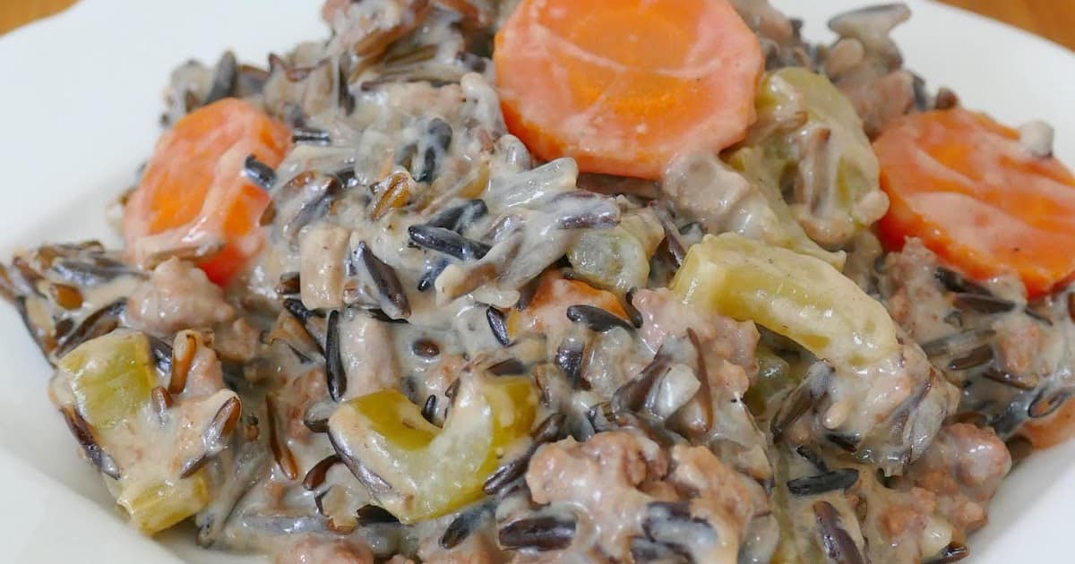 A close-up of a dish featuring wild rice mixed with chunks of meat, sliced carrots, and celery, all coated in a creamy sauce-a perfect addition to your collection of hot dish recipes.