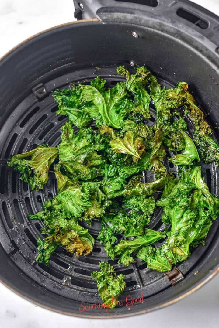 Air fryer kale chips in a black fryer basket, displaying a mix of vibrant green and slightly browned edges.