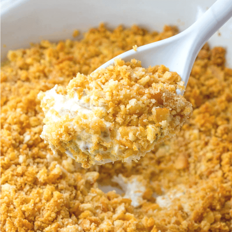 A spoonful of a creamy hot dish topped with golden brown crushed crackers in a white dish.