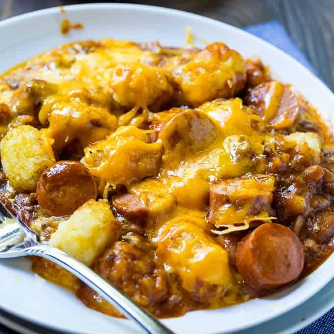 A white plate filled with a cheesy casserole that includes sausage slices and tater tots, accompanied by a fork, perfect for those seeking comforting hot dish recipes.