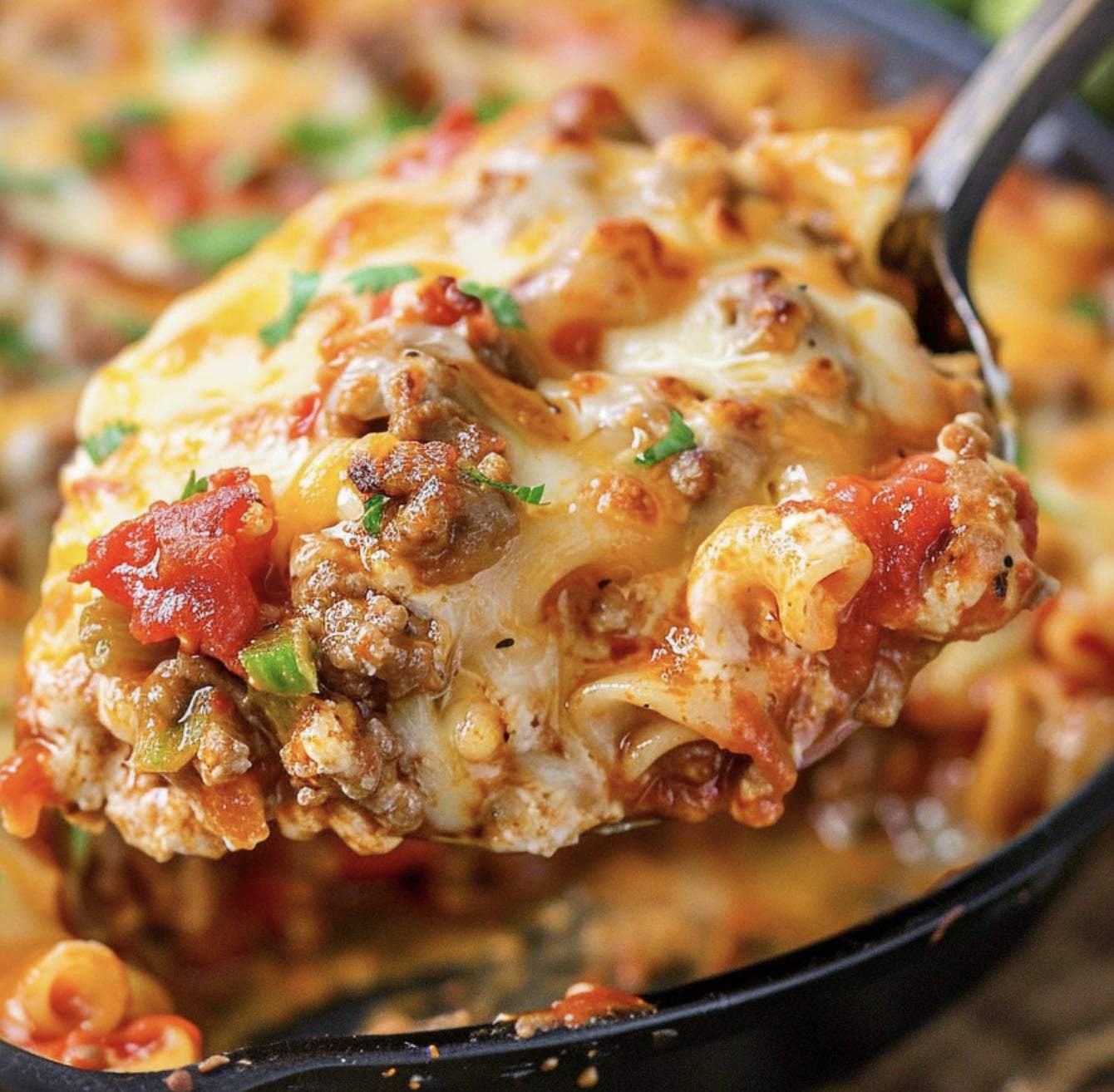 Close-up of a spoonful of cheesy pasta bake with ground meat, tomato sauce, and green bell peppers from a skillet-a perfect addition to your collection of hot dish recipes.