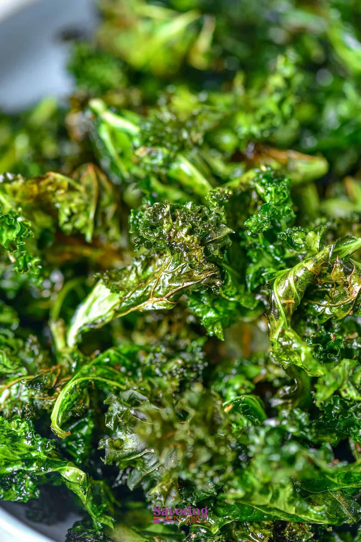 Close-up of crispy, green air fried kale chips with a shiny, slightly crunchy texture. The vibrant colors suggest they are very delicious.