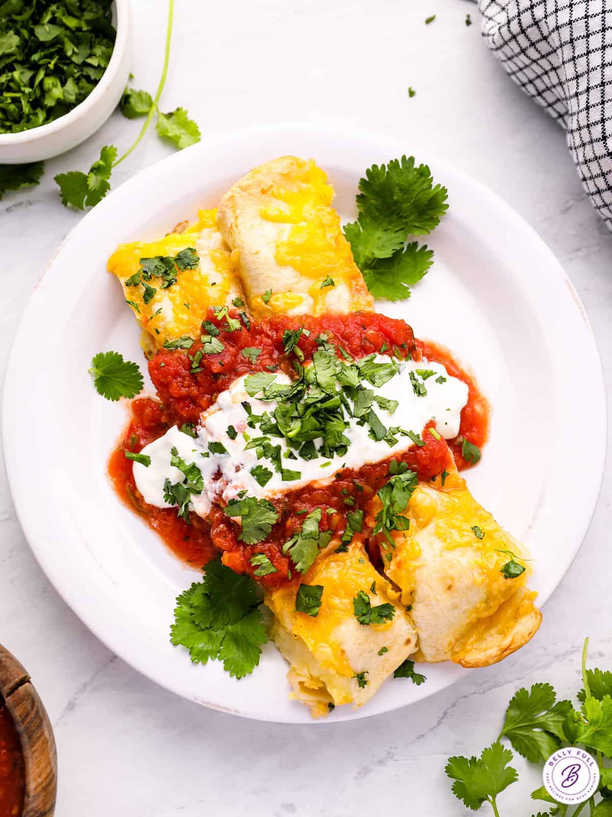 A plate of enchiladas topped with melted cheese, red salsa, and sour cream, garnished with chopped cilantro.