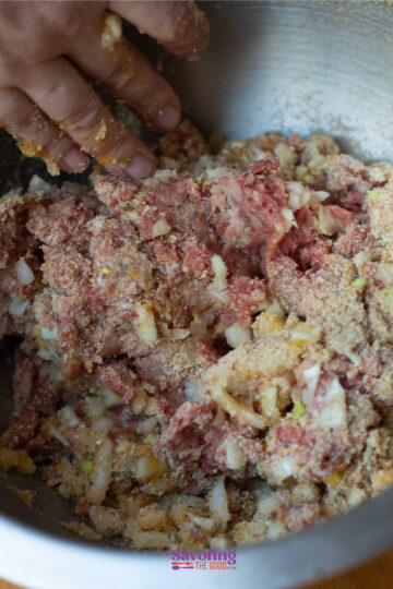 Close-up of a hand mixing ground meat, chopped onions, and breadcrumbs in a metal bowl, reminiscent of preparing homemade IKEA Swedish meatballs.
