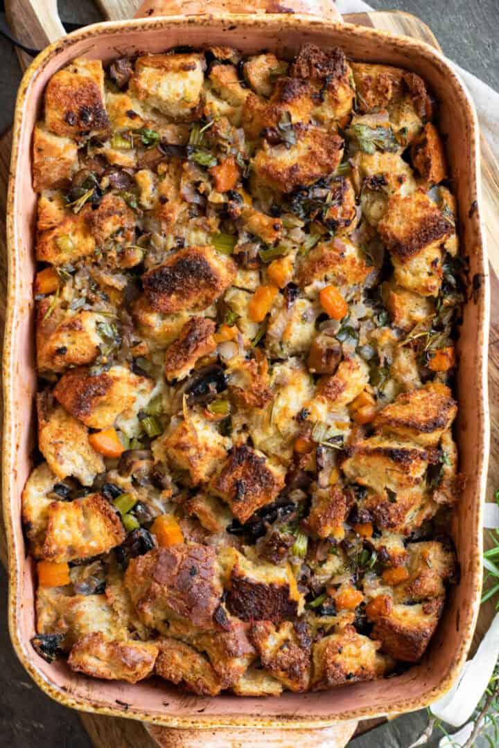 A baked dish of vegetable stuffing featuring browned bread cubes, carrots, onions, celery, and herbs in a rectangular baking dish.