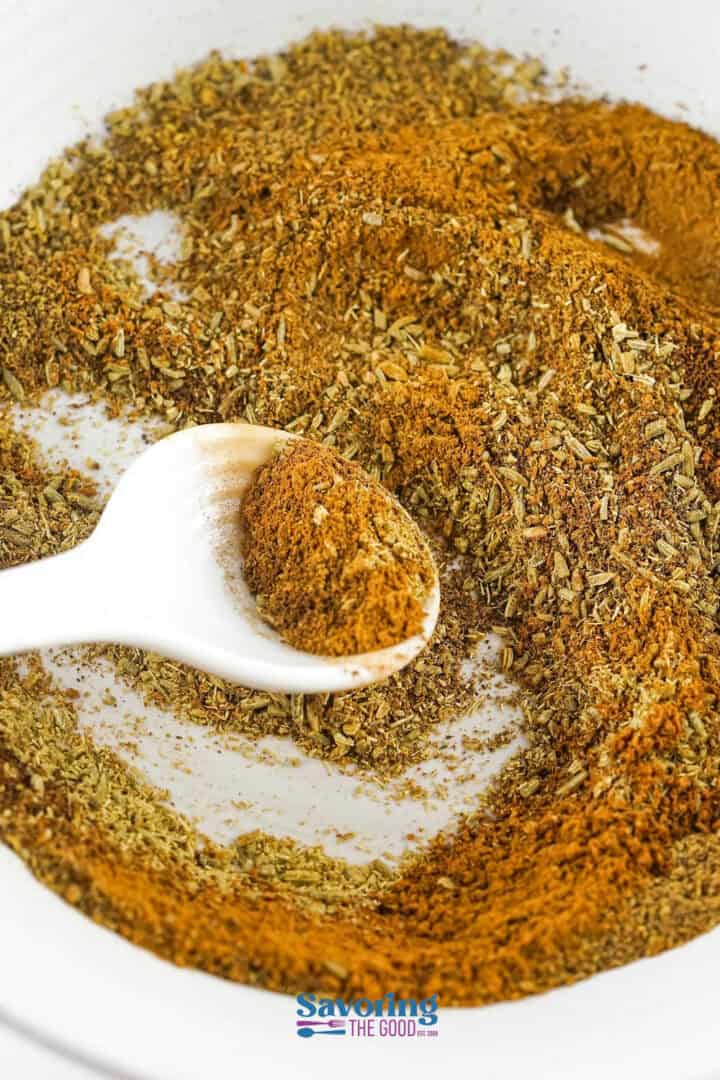 A white spoon is filled with a blend of spices and herbs inside a white bowl. The text "Savoring The Good" is visible at the bottom center of the image.