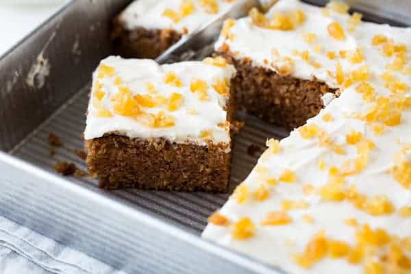 A square slice of cake with white frosting and yellow sprinkles has been cut from a larger cake in a metal baking tray.