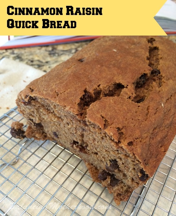 A loaf of cinnamon raisin quick bread with a cracked top rests on a wire cooling rack, showcasing one of the best sweet loaf cake recipes. The yellow label at the top left reads "Cinnamon Raisin Quick Bread".