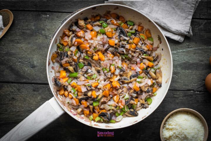 A skillet containing a cooked mixture of diced vegetables, including onions, celery, mushrooms, and carrots, on a wooden surface-a perfect base for your next vegetable stuffing recipe.