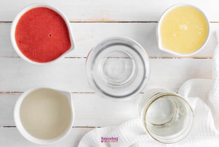 Overhead view of four small bowls containing different colored liquids, a jar of liquid, and a glass bottle on a white wooden tabletop. A white cloth is placed beside the bowls.