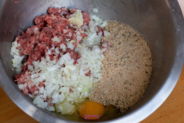 A mixing bowl containing ground meat, chopped onions, breadcrumbs, minced garlic, and a cracked egg — the perfect base for an IKEA Swedish meatballs recipe.