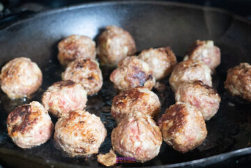 Close-up of several browned meatballs cooking in a black skillet, following an authentic IKEA Swedish meatballs recipe.