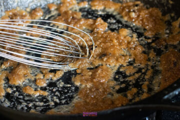 A close-up of a whisk stirring browned butter in a black skillet, reminiscent of the first step in creating the perfect IKEA Swedish meatballs recipe.