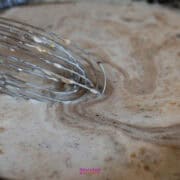 A close-up of a whisk stirring a pot of cream sauce, creating a swirled pattern, reminiscent of preparing an IKEA Swedish meatballs recipe.