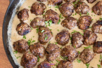 A skillet filled with browned meatballs simmering in a creamy sauce, garnished with chopped parsley, reminiscent of an IKEA Swedish meatballs recipe.