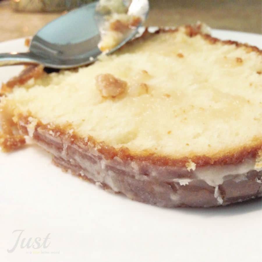A close-up of a slice of sweet glazed lemon loaf cake on a white plate with a spoon resting on top.