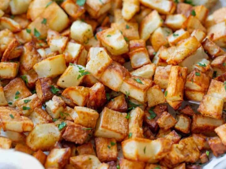 A tray of golden brown roasted potatoes garnished with chopped green herbs.