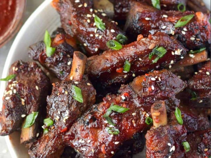 A bowl of glazed pork ribs garnished with green onions and sesame seeds.