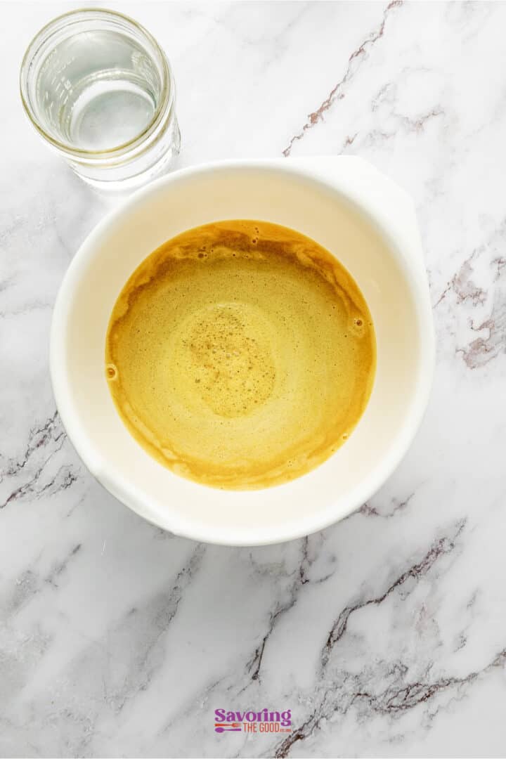 A glass of water, a bowl of frothy coffee, and a refreshing passion fruit juice sit on a white marble countertop.