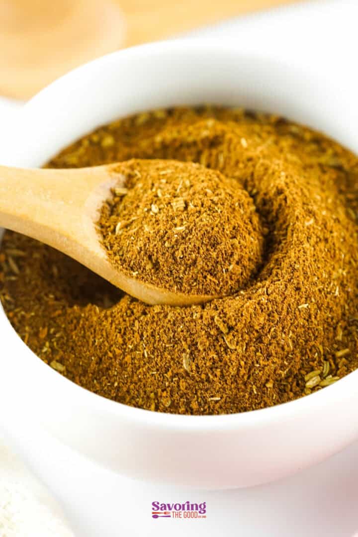 A wooden spoon scooping Chinese five spice from a white bowl.