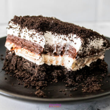 A slice of chocolate lasagna rests on a black plate, boasting creamy layers and a crumbled cookie topping.