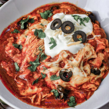 A Crockpot chicken enchilada casserole soup, featuring a hearty bowl of chicken enchilada soup topped with shredded cheese, sour cream, sliced black olives, and cilantro.