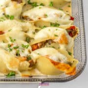 Close-up of Philly Cheesesteak stuffed pasta shells topped with melted cheese and fresh parsley in a glass baking dish.