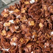 A close-up of golden graham s'mores mingling with chocolate-coated cereal pieces and marshmallows in a glass dish.