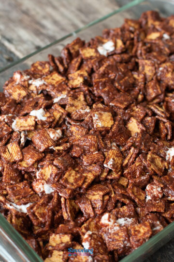 A close-up of golden graham s'mores mingling with chocolate-coated cereal pieces and marshmallows in a glass dish.