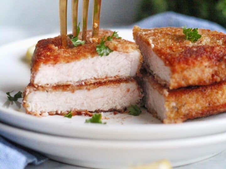 Fork inserted into breaded chicken pieces on a white plate, garnished with parsley. A lemon wedge is in the foreground.