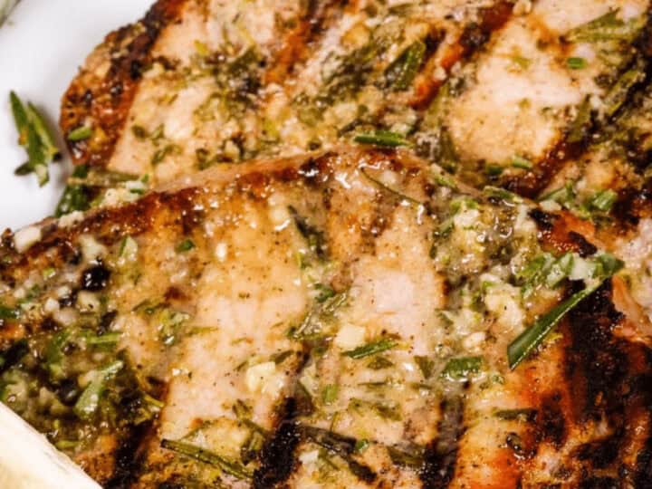 Grilled pork chops seasoned with herbs and garlic, served with a lemon wedge.