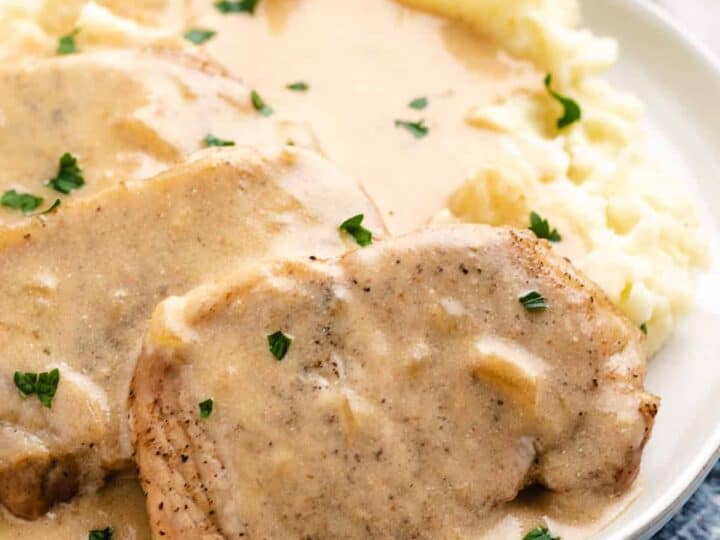 Plate of pork chops with creamy gravy, garnished with parsley, served alongside mashed potatoes.