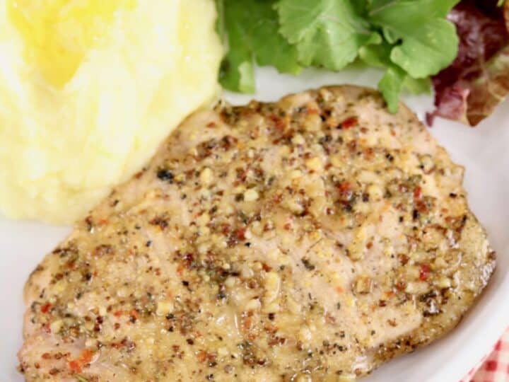 A seasoned grilled chicken breast served on a plate with mashed potatoes and a green salad.