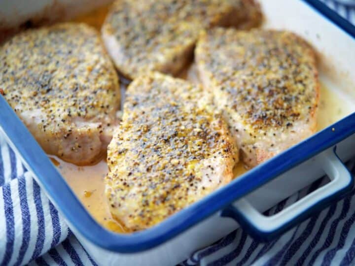 Four seasoned chicken breasts baking in a white rectangular dish on a striped cloth.
