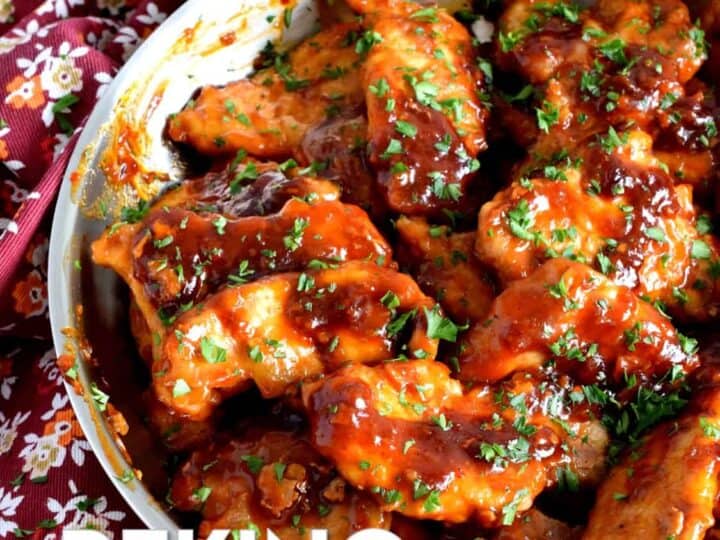 A skillet filled with Peking pork chops garnished with herbs, placed on a floral tablecloth.