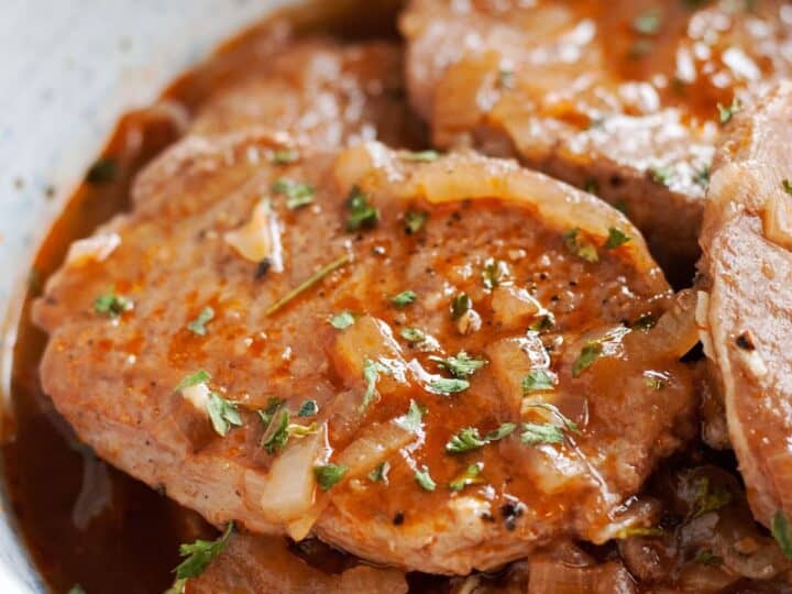 Close-up of cooked pork chops with onions and herbs in a savory sauce.