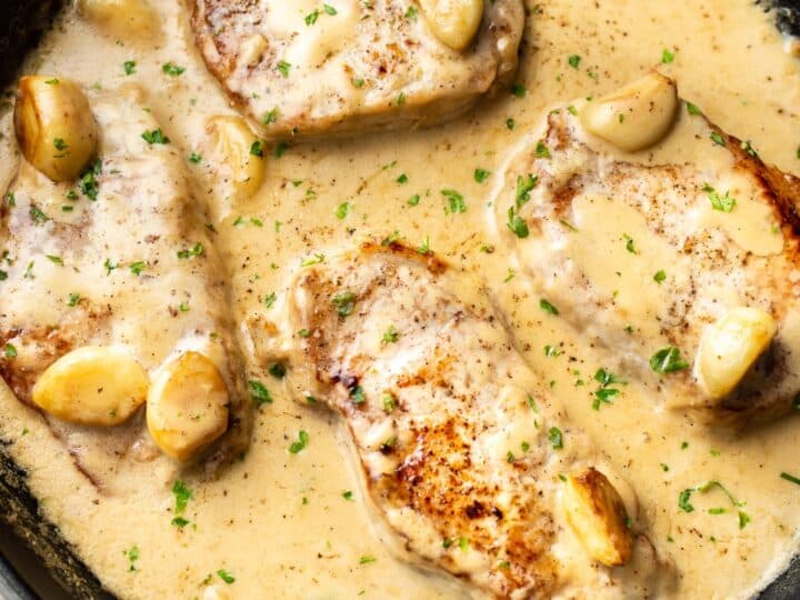 Pork chops in a creamy garlic sauce with herbs, cooked in a black skillet.