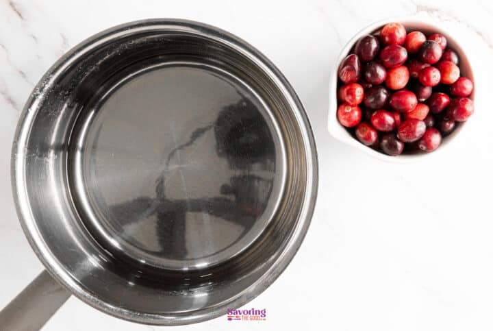 A stainless steel pot sits next to a bowl of sugared cranberries on a marble countertop.