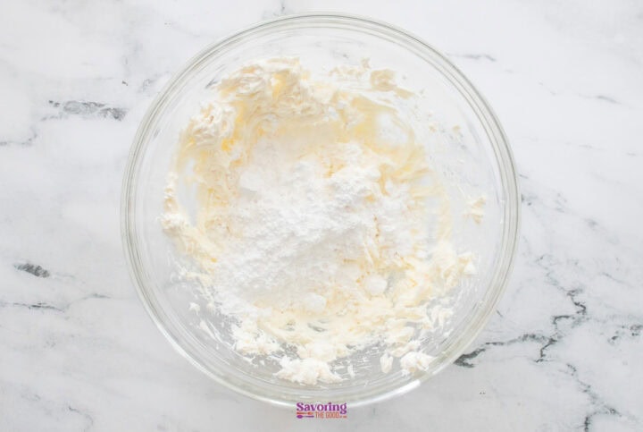 A glass bowl containing a creamy mixture of whipped cream and powdered sugar sits on a marble surface, ready to be layered into a decadent chocolate lasagna.