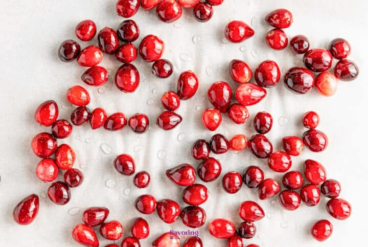 Sugared cranberries glisten as they lie scattered on a white surface, adorned with delicate droplets of sugar syrup.