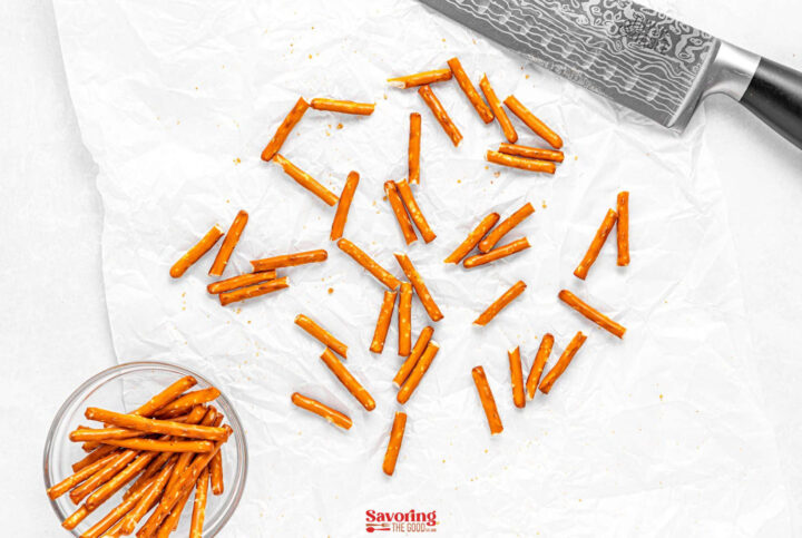Acorn cookies and pretzel sticks are scattered on white parchment paper, with a knife in the top right corner and a small bowl of pretzels in the bottom left.