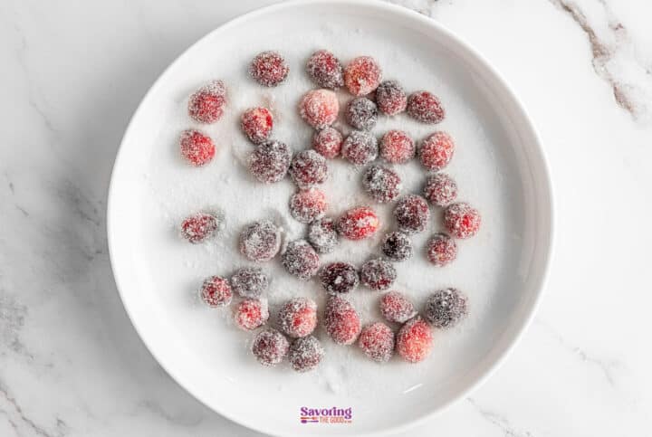 A white plate showcases a delightful arrangement of sugared cranberries, glistening invitingly on a marble surface.