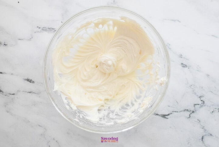 A clear glass bowl with creamy, whipped white frosting sits on a marble surface, reminiscent of layers in a decadent chocolate lasagna.
